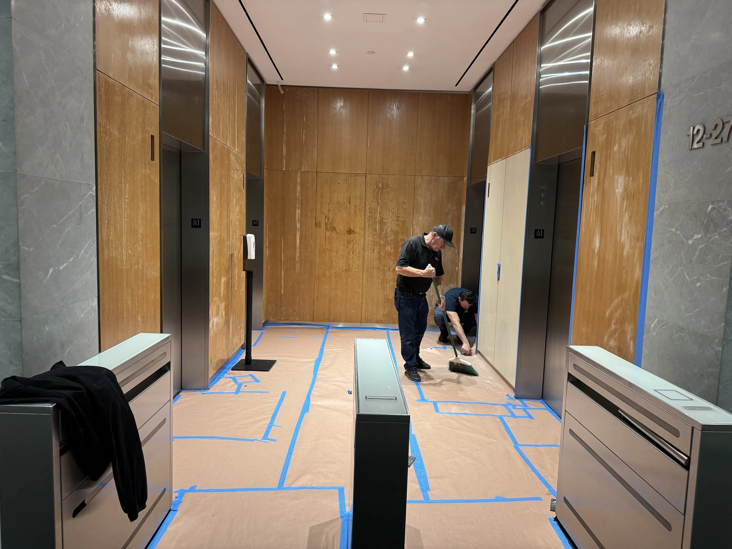 Luxor technicians cleaning an elevator lobby with protective paper still in place
