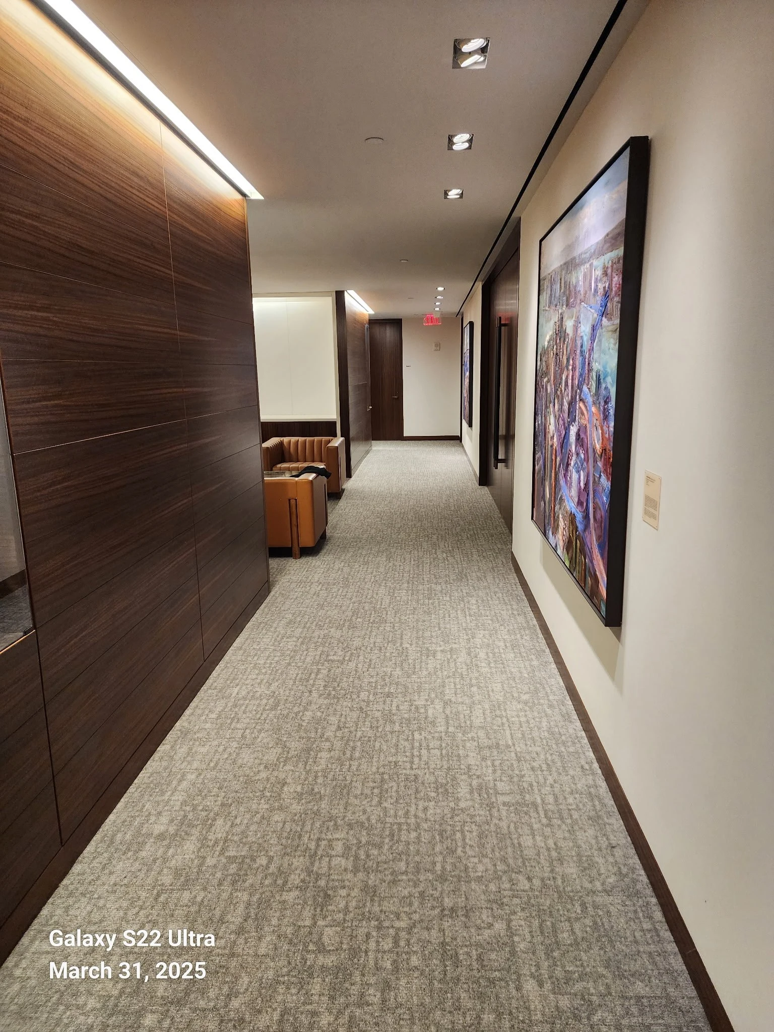 Walnut paneling, carefully lit artwork and carpet in a professional office corridor